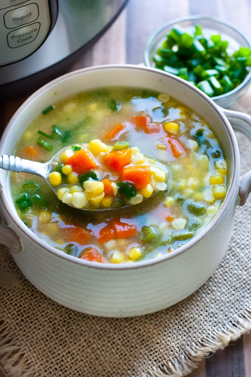 A spoon lifts vibrant corn and carrot soup from a white bowl on a burlap mat.