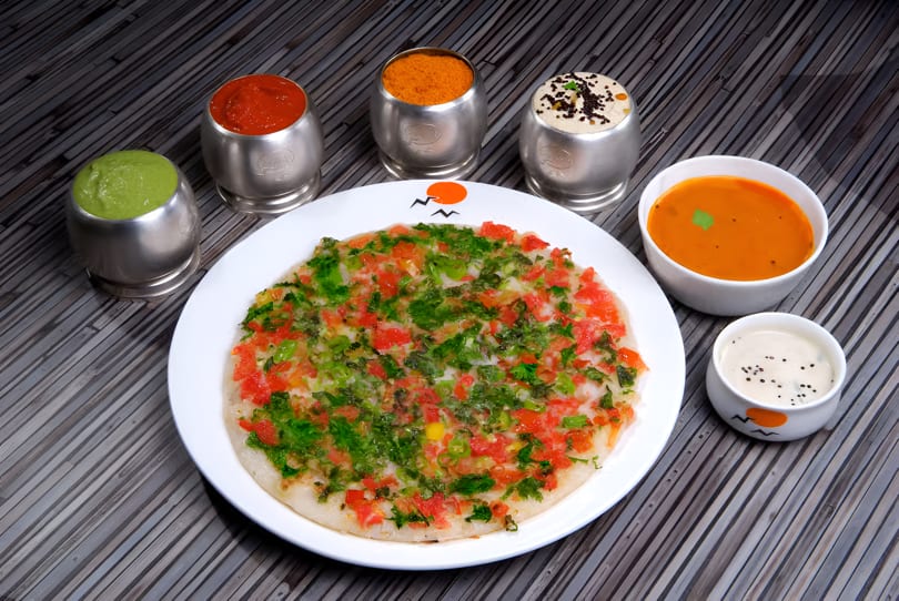 Savory uttapam topped with tomatoes and herbs, served with various chutneys and sambar.