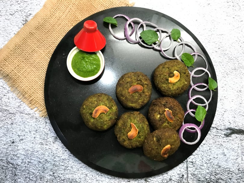 Six green patties topped with cashews, served with green chutney, onion rings, and mint.