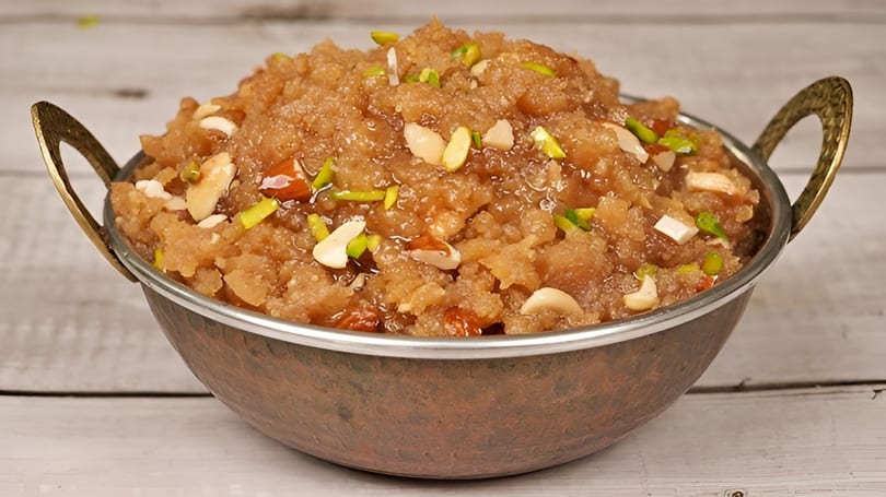 A copper bowl filled with halwa, garnished with slivered almonds, cashews, and pistachios.